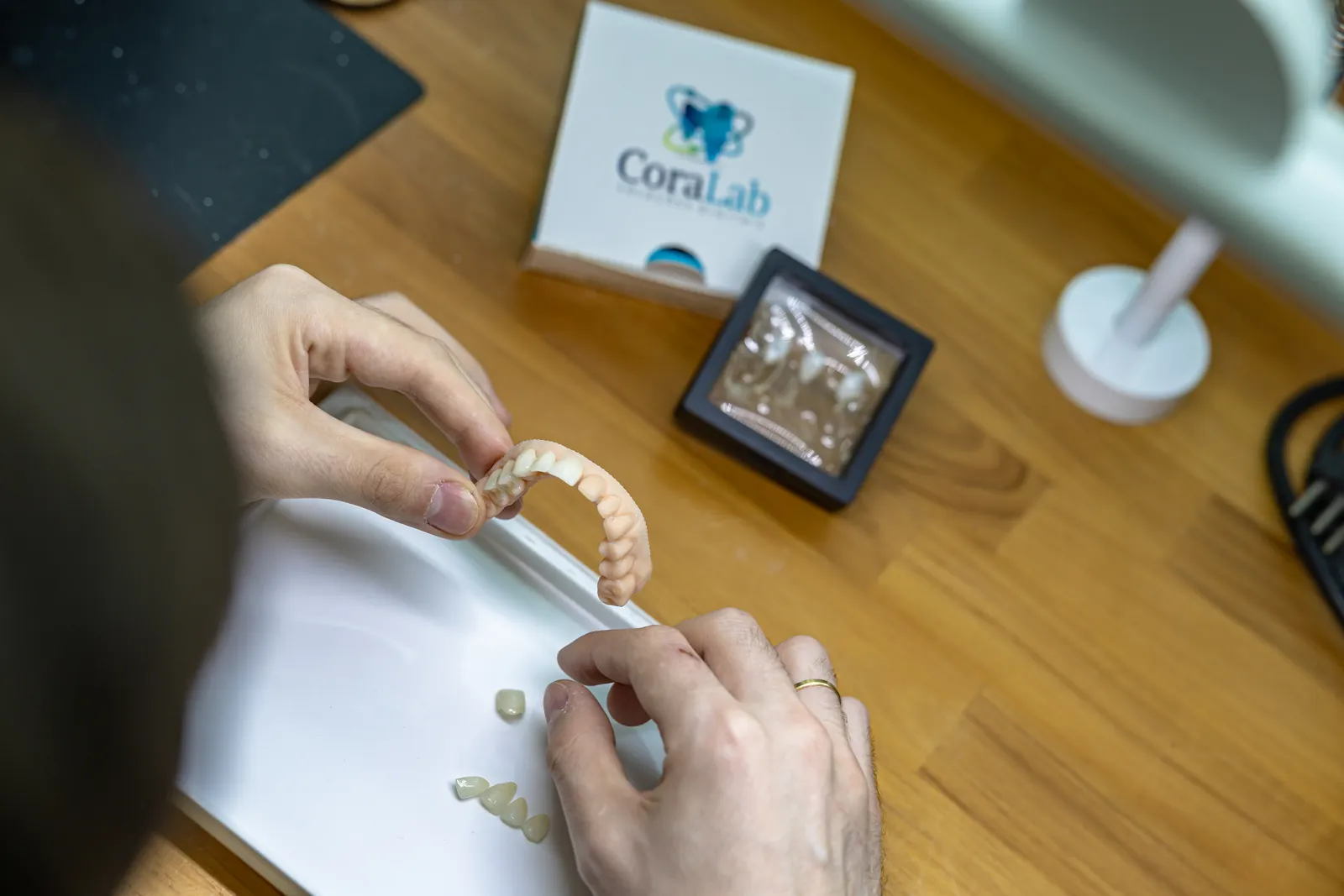 Mãos segurando prótese dentária finalizada no laboratório Coralab
